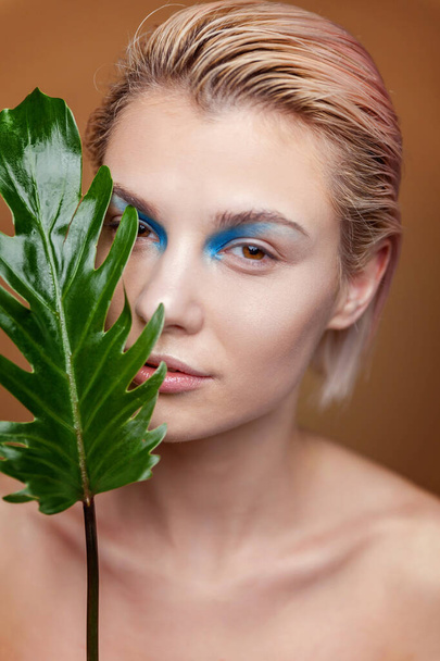 Ομορφιά πορτρέτο της νεαρής ξανθιάς γυναίκας με τέλεια μόδα του δέρματος συνθέτουν και πράσινο φύλλο σε φυσικό καφέ φόντο. Cleansing eco organic cosmetic χαλαρώστε και περιποιηθείτε. Spa και ευεξία - Φωτογραφία, εικόνα