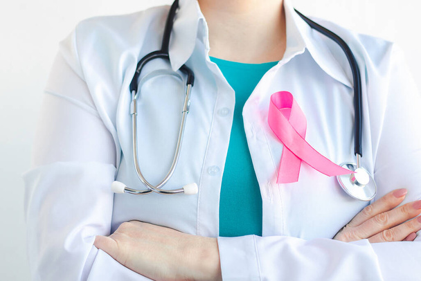 Vrouwelijke dokter in medisch wit uniform met roze lint. Borstkankerbewustmakingsmaand. Gezondheidsconcept voor vrouwen. Symbool van hoop en steun. Campagne ter bestrijding van kanker. - Foto, afbeelding