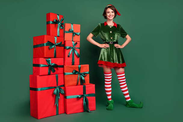 Photo of cheerful delivery helper lady pile presents wear elf costume hat stockings isolated green color background - Valokuva, kuva