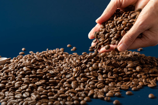 Hands pouring coffee beans on the table. Coffee scattered on the table. Blue background. Close-up. Copy space. - Φωτογραφία, εικόνα