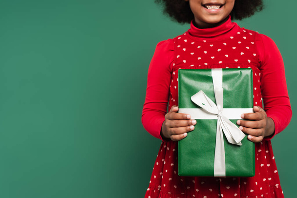 Cropped view of smiling african american child holding present with ribbon isolated on green  - Photo, Image