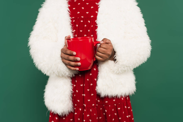 Cropped view of african american girl in fluffy jacket holding cup isolated on green  - Foto, immagini