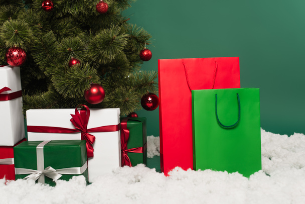 Regali vicino a borse della spesa, neve decorativa e albero di Natale su sfondo verde  - Foto, immagini