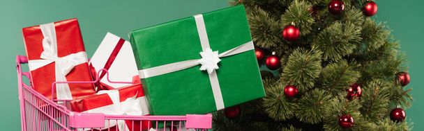 Gifts in shopping cart near decorated christmas tree isolated on green, banner  - Foto, immagini