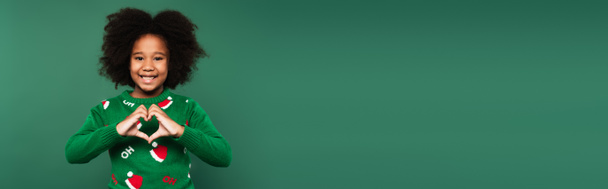 Африканский американец в свитере показывает жест любви изолирован на зеленый, баннер  - Фото, изображение