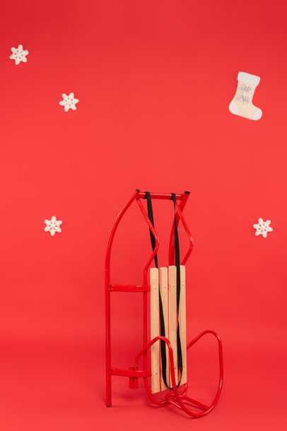 Сани возле декоративных снежинок на красном фоне - Фото, изображение