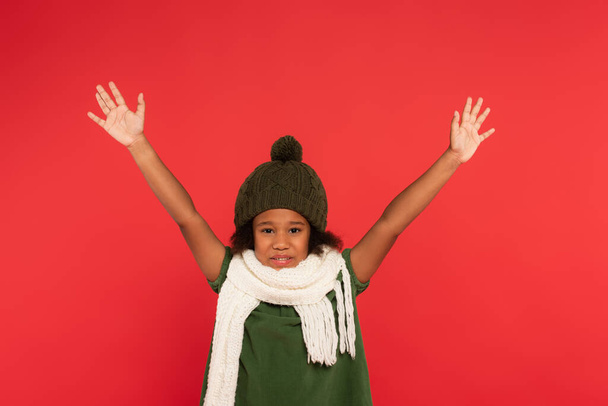 Criança afro-americana em chapéu e cachecol acenando as mãos na câmera isolada no vermelho  - Foto, Imagem