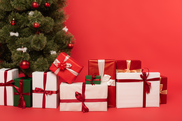 赤い背景に飾られたクリスマスツリーの近くのプレゼント - 写真・画像