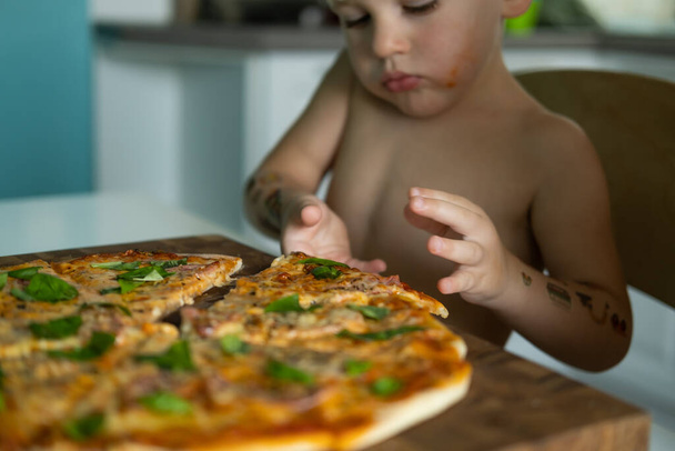 słodkie dziecko chłopiec jedzenie w domu pizzy w kuchni w domu. - Zdjęcie, obraz