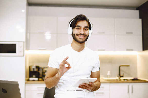 Online education. Young arabic man study with a tablet at home and taking notes. - 写真・画像