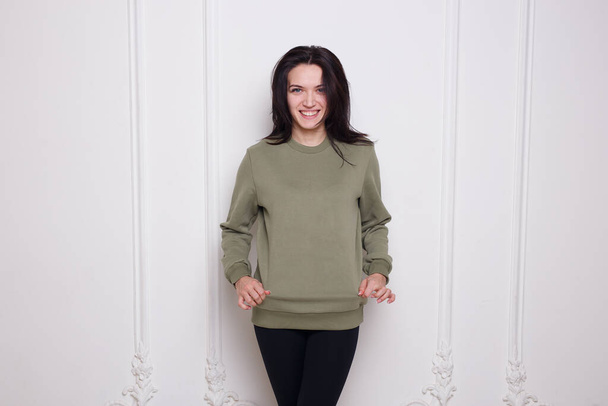 Smiling young woman brunette in a geen sweater, looking at camera, isolated on white background. Space copy. - Foto, Bild