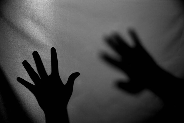 Il concetto dell'ombra della mano dietro il tessuto illuminato da dietro. Halloween sfondo. - Foto, immagini