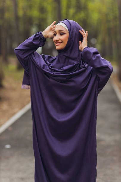 Islamic beautiful woman in a Muslim dress standing on a summer park street background forest autumn trees.world hijab day. - Fotó, kép