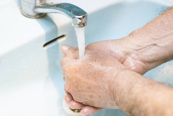 Adam ellerini banyoda sabunla yıkıyor. Corona virüsü enfeksiyonuna karşı en iyi korunma yöntemi. Corona virüsü sık sık ellerini temizleyerek pandemik koruma sağlıyor.. - Fotoğraf, Görsel
