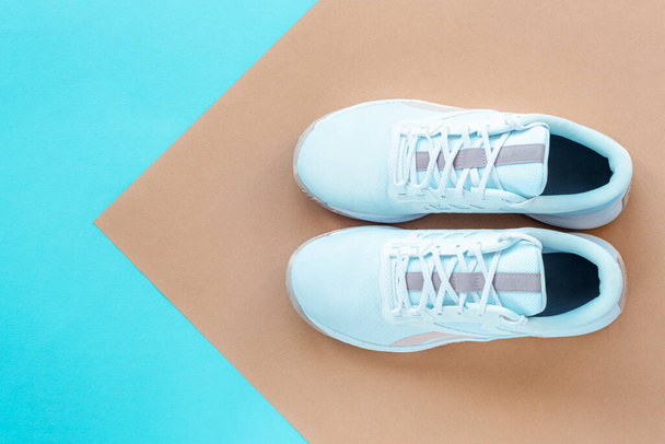 Witte sneakers op blauwe en pastel beige achtergrond. Sport en fitness concept. Bovenaanzicht, vlak lay. - Foto, afbeelding
