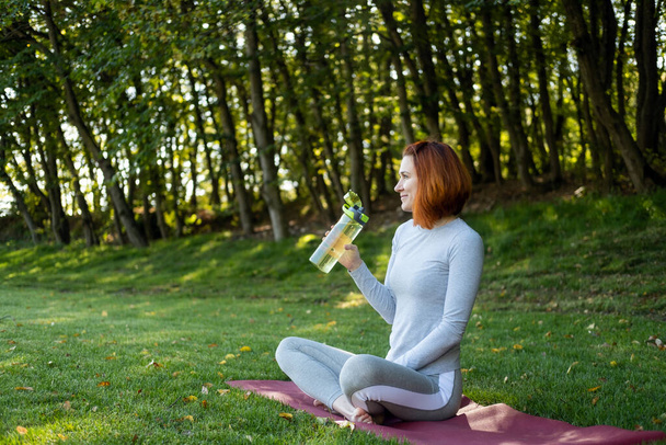 femme en forme en vêtements de sport boire de l'eau tout en faisant du yoga sur le parc en automne journée ensoleillée. - Photo, image