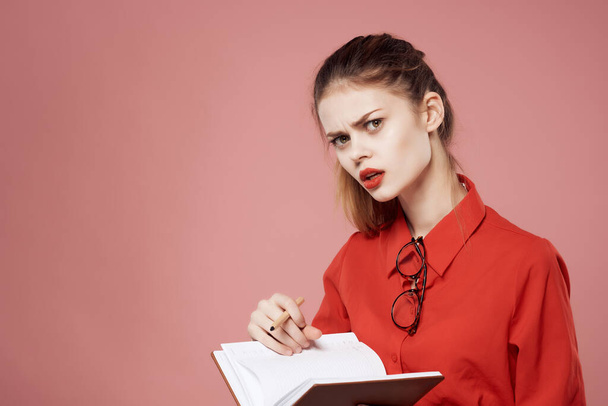 Zakelijke vrouw in rood shirt met notitieblok in handen van werk professionals roze achtergrond - Foto, afbeelding