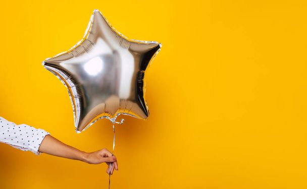 Young female hand holds a bright balloon in the shape of a star on the yellow background - Fotoğraf, Görsel