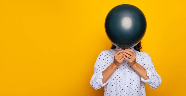 Young girl covered her face with help of black balloon isolated on yellow background - Foto, Bild