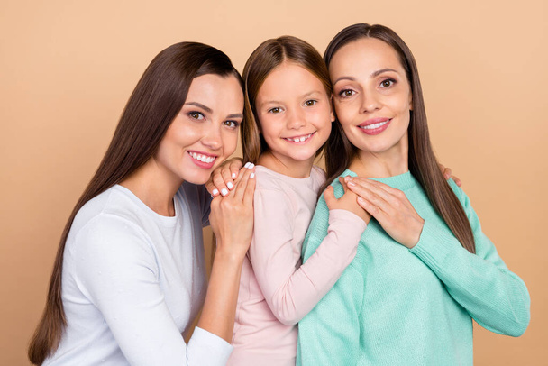 Portrait of three attractive cheerful careful brown-haired girls hugging isolated over beige pastel color background - Fotografie, Obrázek