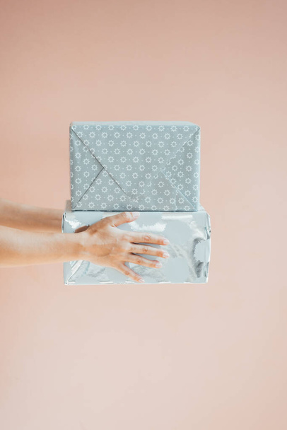 Close Up Photo of a Female Hands Holding Christmas Presents. Unrecognizable young woman giving two big wrapped Christmas gifts over a pink background with copy space. - Photo, Image