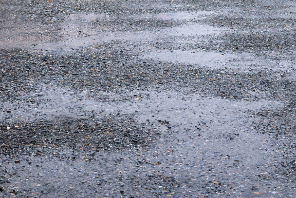 Een foto van het wegdek bedekt met zwarte stenen, als het regent, is er water op de weg. Geschikt voor een gestructureerde achtergrond afbeelding met mooie strepen van water. - Foto, afbeelding