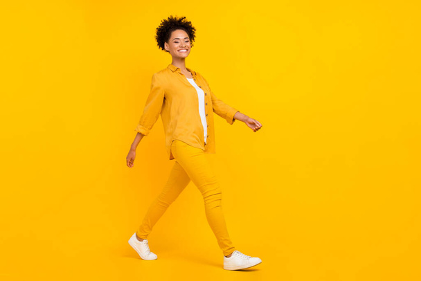 Повнорозмірна фотографія профілю молодої прекрасної афро-жінки йде на зустріч ізольовано на жовтому кольоровому фоні
 - Фото, зображення