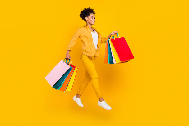 Full body profile side photo of young afro girl jump go walk shop sale bag store isolated over yellow color background - Фото, зображення