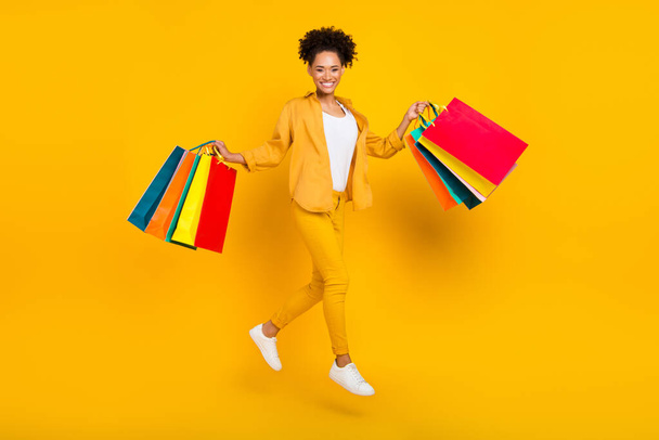 Фотография женщины в полный рост, прыгающей с сумками в продаже изолированный яркий желтый цветовой фон - Фото, изображение