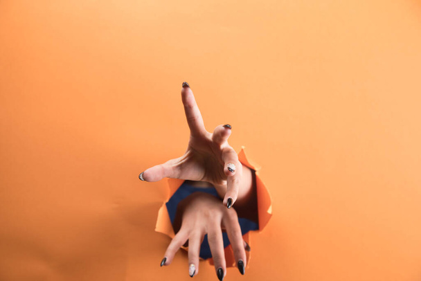 женская рука рвет оранжевую бумагу - Фото, изображение