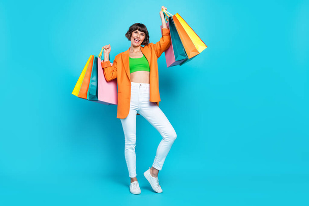 Full size photo of cool young brunette lady hold bags wear blazer top jeans shoes isolated on teal background - Φωτογραφία, εικόνα
