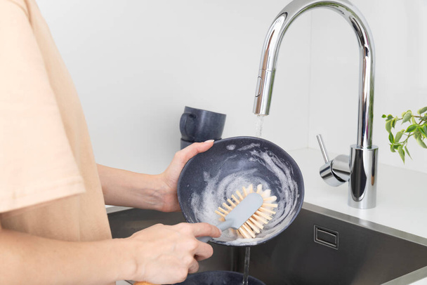 Mujer joven lava platos con cepillo con cerdas naturales en la cocina. Concepto de cero residuos. Foto de alta calidad - Foto, imagen