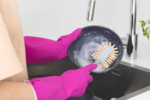 Großaufnahme von weiblichen Händen in rosa Gummihandschuhen, die den Teller mit der Spülbürste waschen. Hochwertiges Foto - Foto, Bild