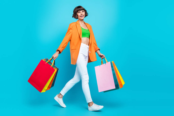 Full length photo of happy woman hold hands shopping bags walk smile isolated on pastel blue color background - Φωτογραφία, εικόνα