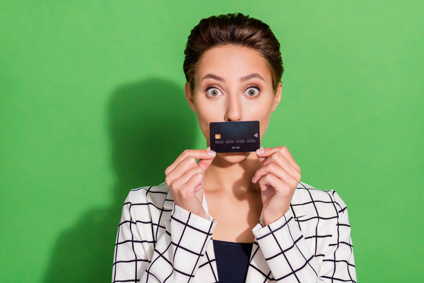 Foto de brilhante impressionado jovem senhora desgaste xadrez roupa cartão de crédito tampa lábios isolado cor verde fundo - Foto, Imagem