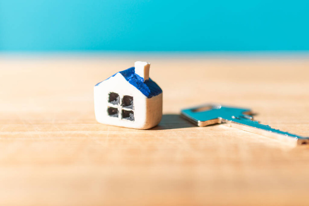 Miniatuur nieuw huis met huissleutel op houten blauwe wazig achtergrond, vastgoed en onroerend goed zakelijke concept.Close-up, selectieve focus. - Foto, afbeelding