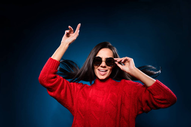 Photo of funky pretty young lady wear knitted sweater dark glasses smiling dancing isolated gradient blue color background - 写真・画像