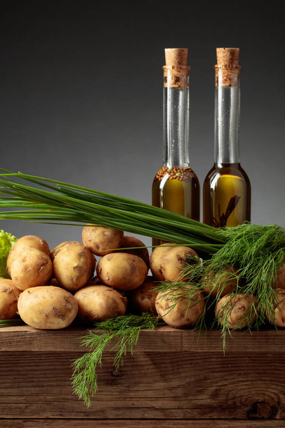 Fresh potatoes with vegetable oil, dill, and onion on a old wooden table. Copy space. - Fotoğraf, Görsel
