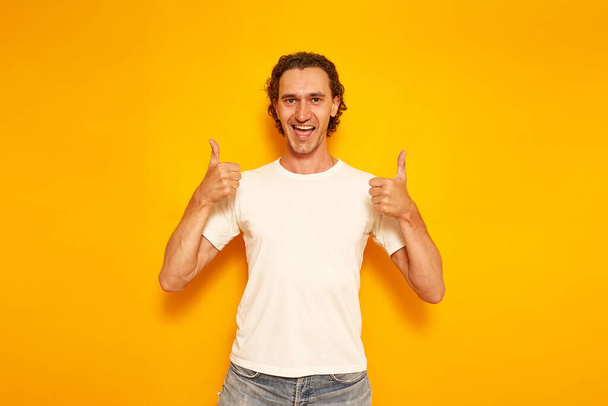 young excited man in casual clothes shows thumbs up with both hands with his mouth open happiness. isolated yellow background. space for text. concept - people, good news, promotions, discounts, likes - Fotografie, Obrázek