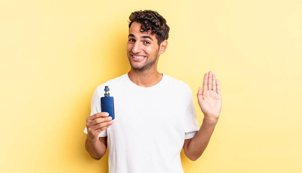 hispanic handsome man smiling happily, waving hand, welcoming and greeting you. vaporizer concept - 写真・画像