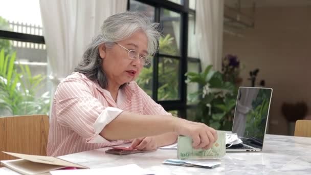 Aasian vanhukset nainen Istu ja laskea Thaimaan baht ansainnut työstä. talouslukutaidon käsite eläkkeellä, säästöissä, vakuutuksissa, eläkkeissä - Materiaali, video