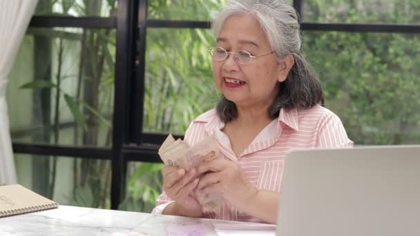 Eine asiatische ältere Frau sitzt und zählt den thailändischen Baht, den sie bei der Arbeit verdient hat. Konzept der Finanzkompetenz im Ruhestand, Ersparnisse, Versicherungen, Rente - Filmmaterial, Video