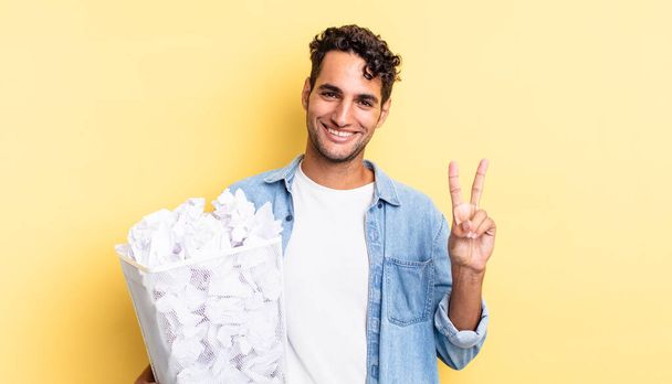 hispanic handsome man smiling and looking friendly, showing number two. paper balls trash concept - Photo, image
