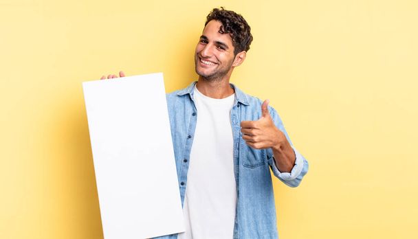 hispanic handsome man feeling proud,smiling positively with thumbs up. empty canvas concept - Fotoğraf, Görsel