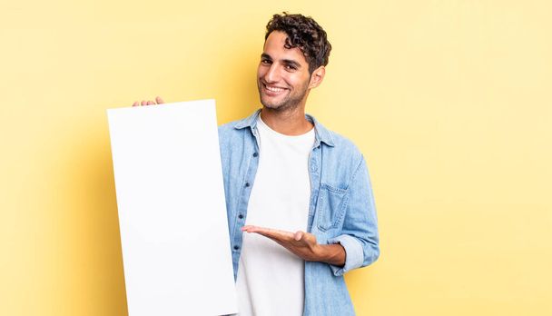 hispanic handsome man smiling cheerfully, feeling happy and showing a concept. empty canvas concept - Fotoğraf, Görsel