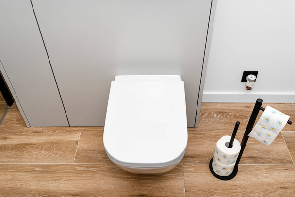 A white ceramic toilet with an closed flap in a modern bathroom, a floor covered with ceramic tiles imitating wood. - Foto, imagen