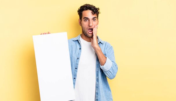 hispanic handsome man feeling shocked and scared. empty canvas concept - Photo, Image