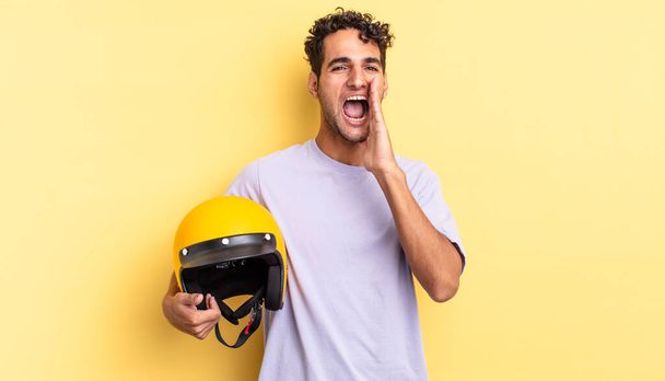 hispanic handsome man feeling happy,giving a big shout out with hands next to mouth. motorbike helmet concept - Foto, imagen