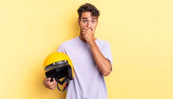 hispanic handsome man covering mouth with hands with a shocked. motorbike helmet concept - Fotografie, Obrázek