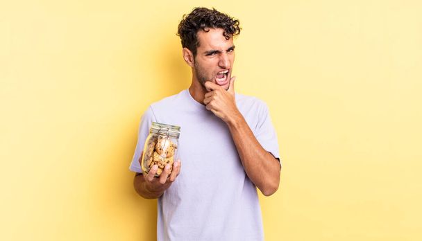 hispanic handsome man with mouth and eyes wide open and hand on chin. cookies concept - Photo, Image